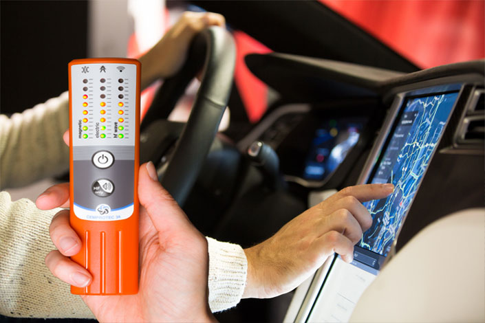 Eine Hand hält das Cemprotec-Elektrosmogmessgerät in einem Auto.